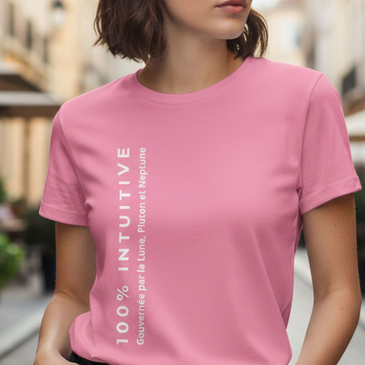 T-shirt Femme Triplicité d'Eau "100% Intuitive – Gouvernée par la Lune, Pluton et Neptune" Une jeune femme portant un t-shirt rose avec un texte blanc vertical. L'inscription principale indique « 100% Intuitive», accompagnée de la mention plus petite «Gouvernée par la Lune, Pluton et Neptune». La scène est capturée en extérieur avec un arrière-plan lumineux et flou.
