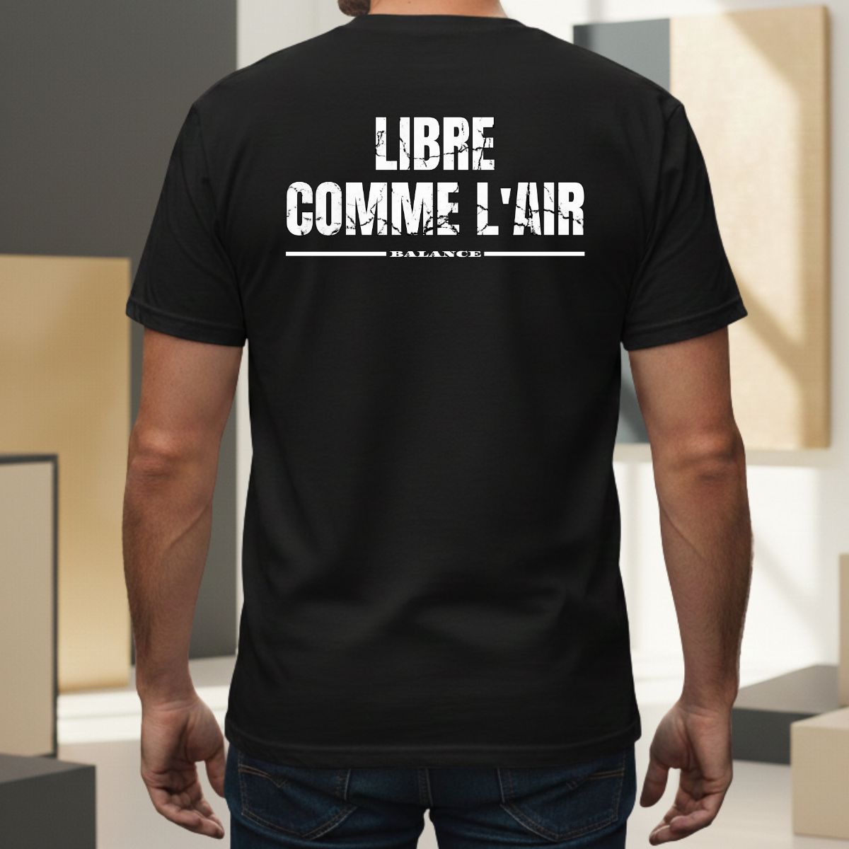 T-shirt Manches Courtes | Libre comme l'Air | Balance : Élément Air T-shirt noir pour homme avec mention 'balance' soulignée. Design graphique au style usé/vintage centré dans le dos, porté par un modèle masculin dans un cadre extérieur moderne.
